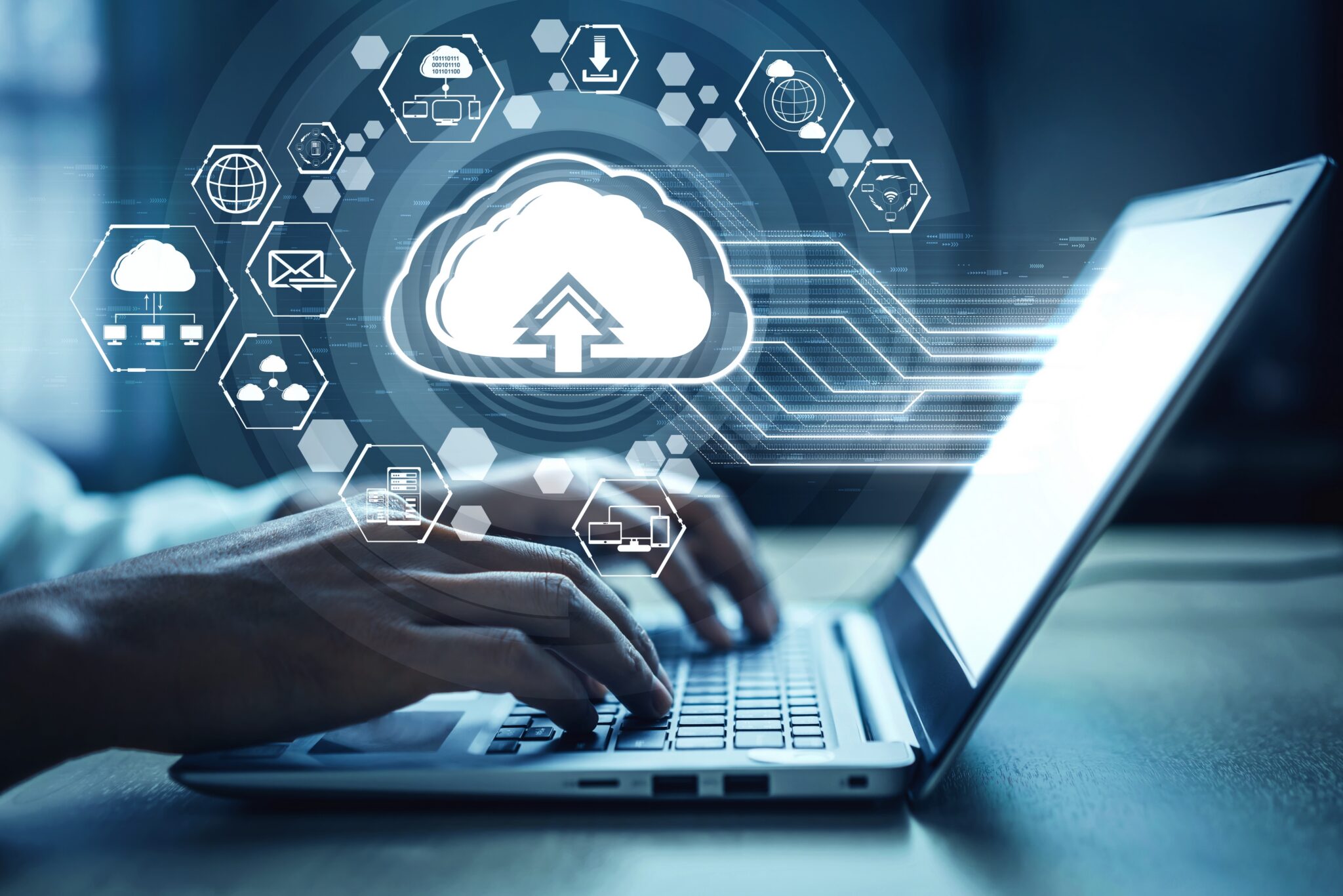 Person typing on a laptop with a large cloud icon and floating tech icons above, symbolizing cloud computing.